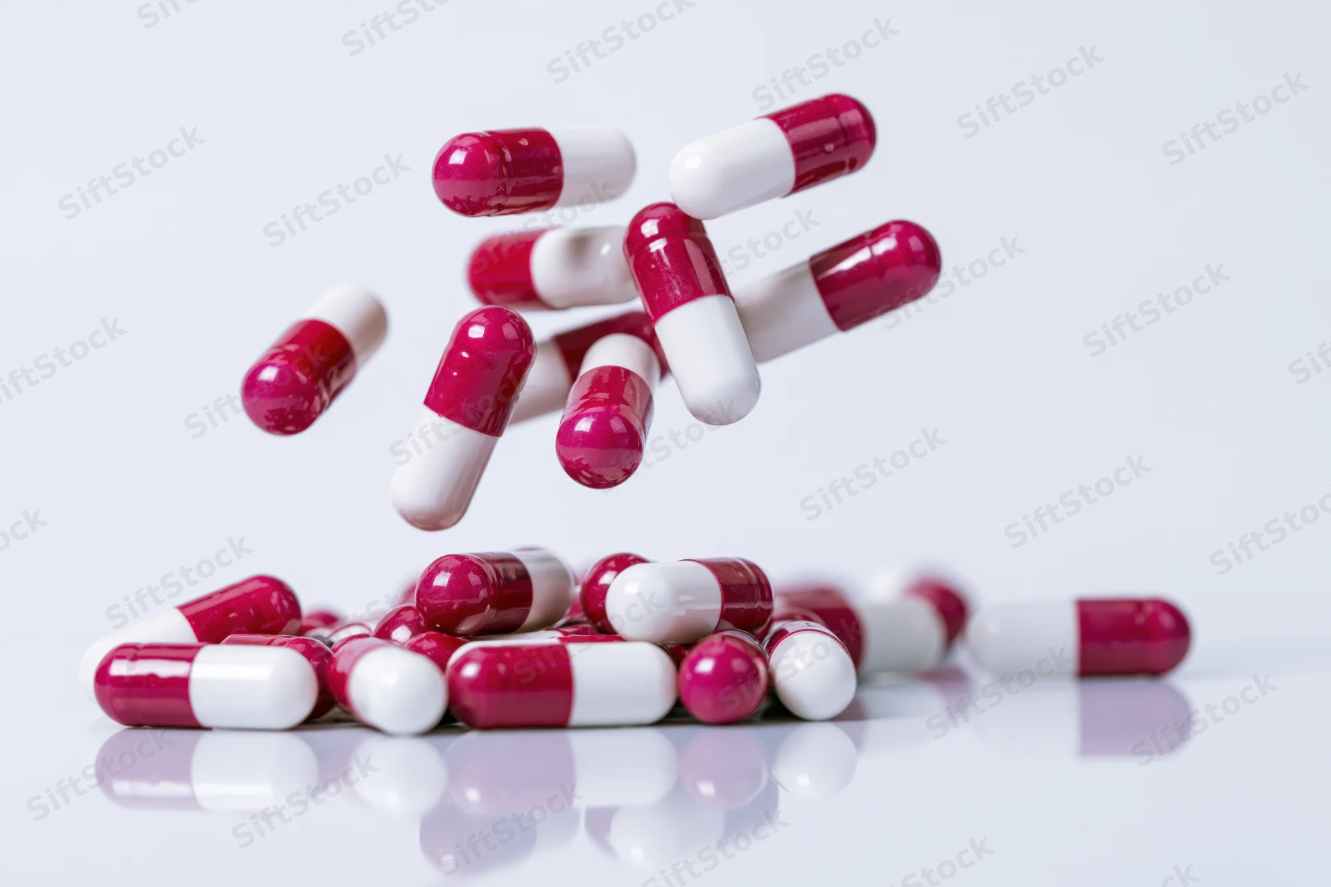 Red and white gelatin capsules falling and scattering on a reflective white surface
