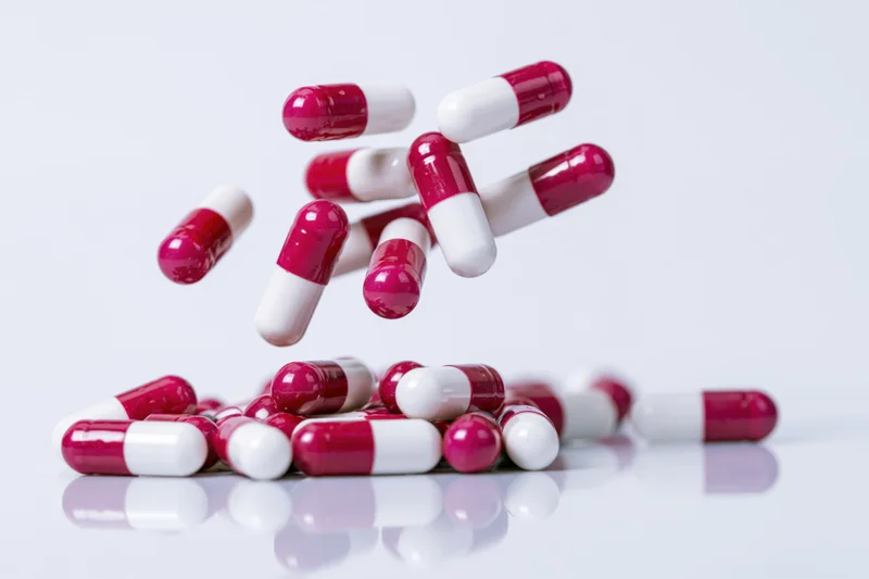 Red and white gelatin capsules falling and scattering on a reflective white surface
