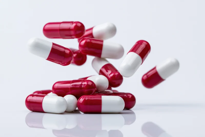 Red and white gelatin capsules falling and scattering on a reflective white surface