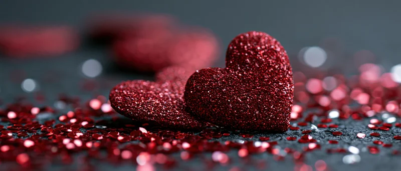 Red glitter hearts resting on dark surface scattered with sequins