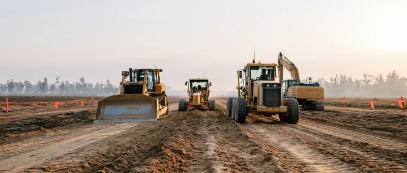 Bulldozers and excavators grading dirt at a road construction site during twilight