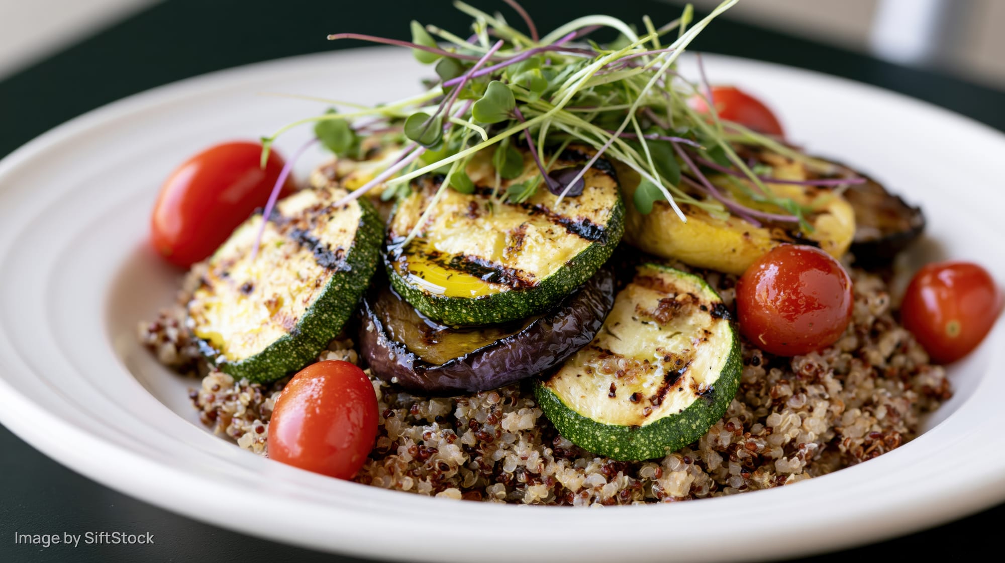 Grilled vegetables and quinoa salad served on a white ceramic plate with microgreens and cherry tomatoes