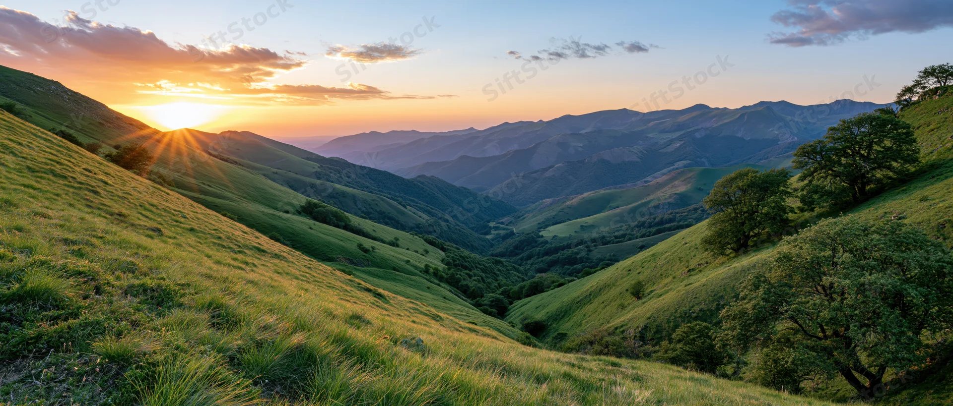 Rolling green hillsides at sunset with sunbeams over a mountain valley
