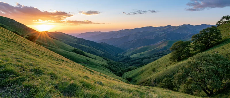 Rolling green hillsides at sunset with sunbeams over a mountain valley