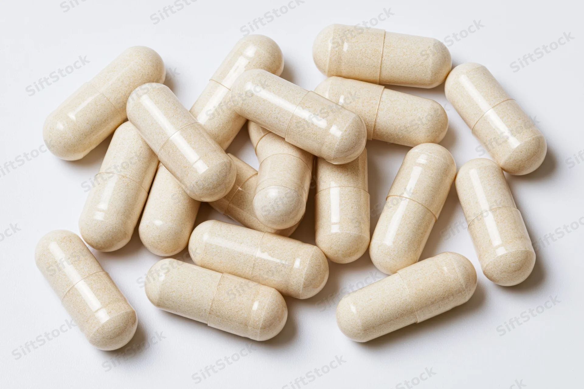 Beige supplement capsules scattered loosely on white background