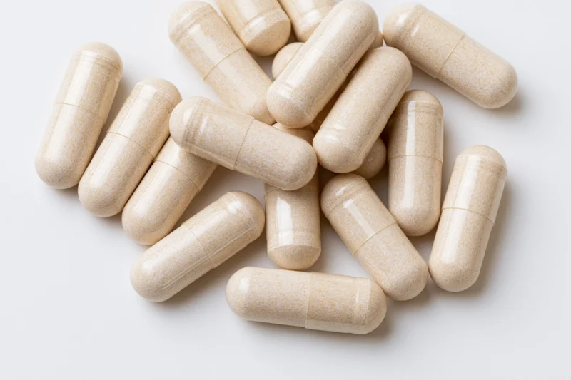 Beige supplement capsules scattered on white surface