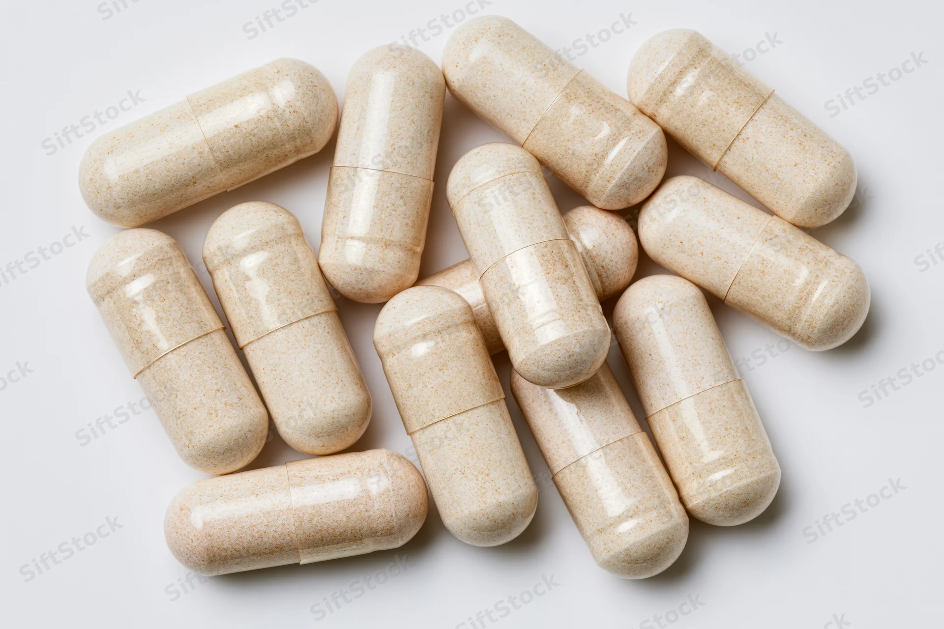 Beige supplement capsules scattered on white surface