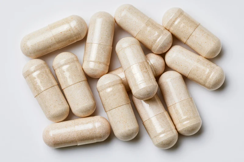 Beige supplement capsules scattered on white surface