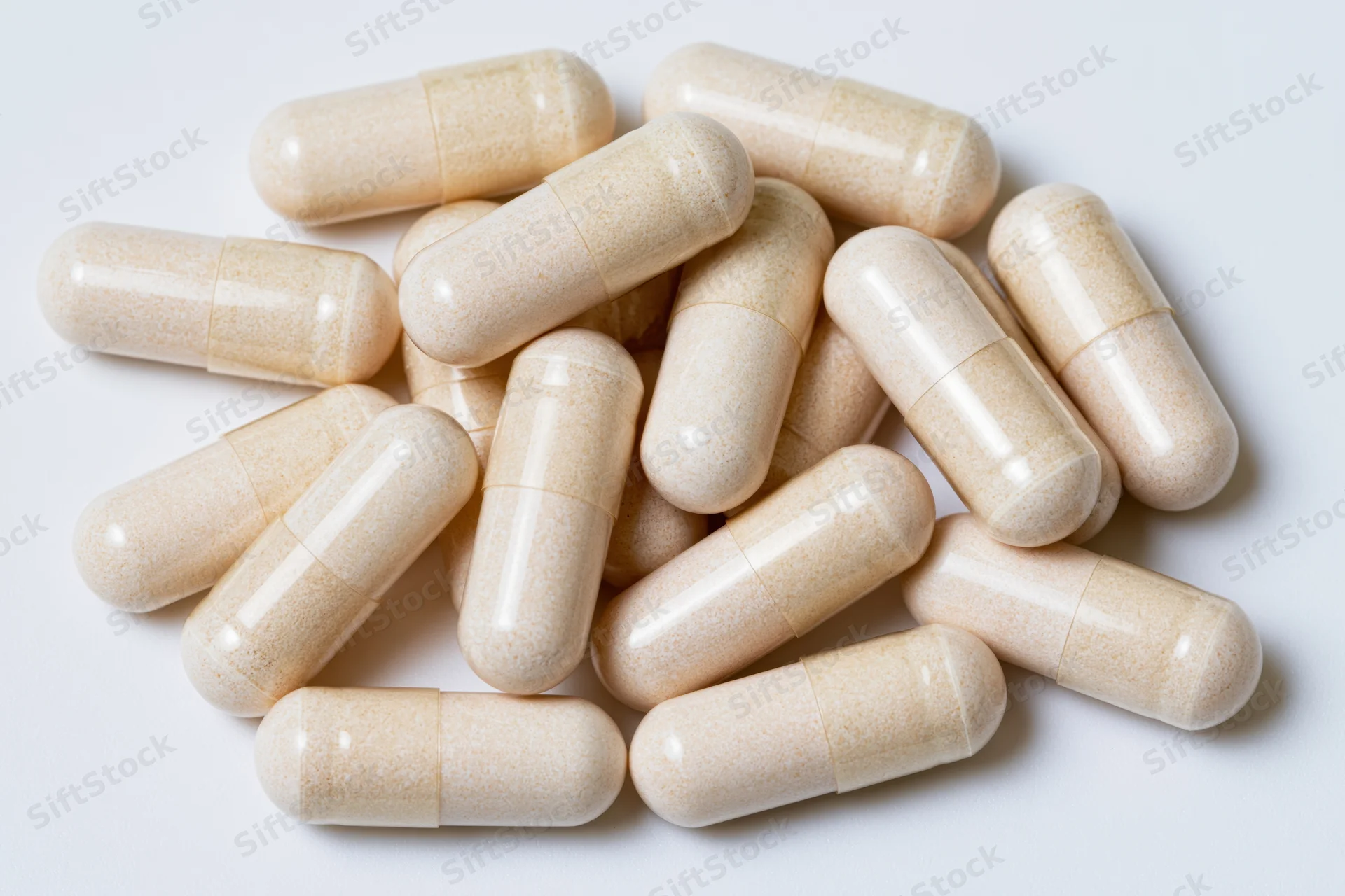 Beige supplement capsules scattered on white surface