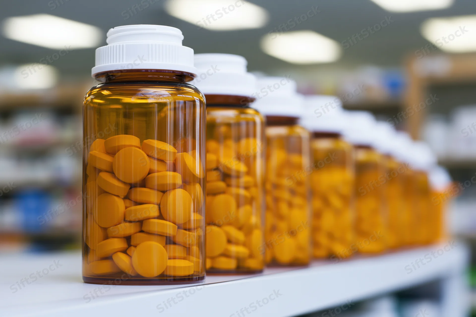 Row of amber prescription bottles filled with orange tablets on a pharmacy shelf