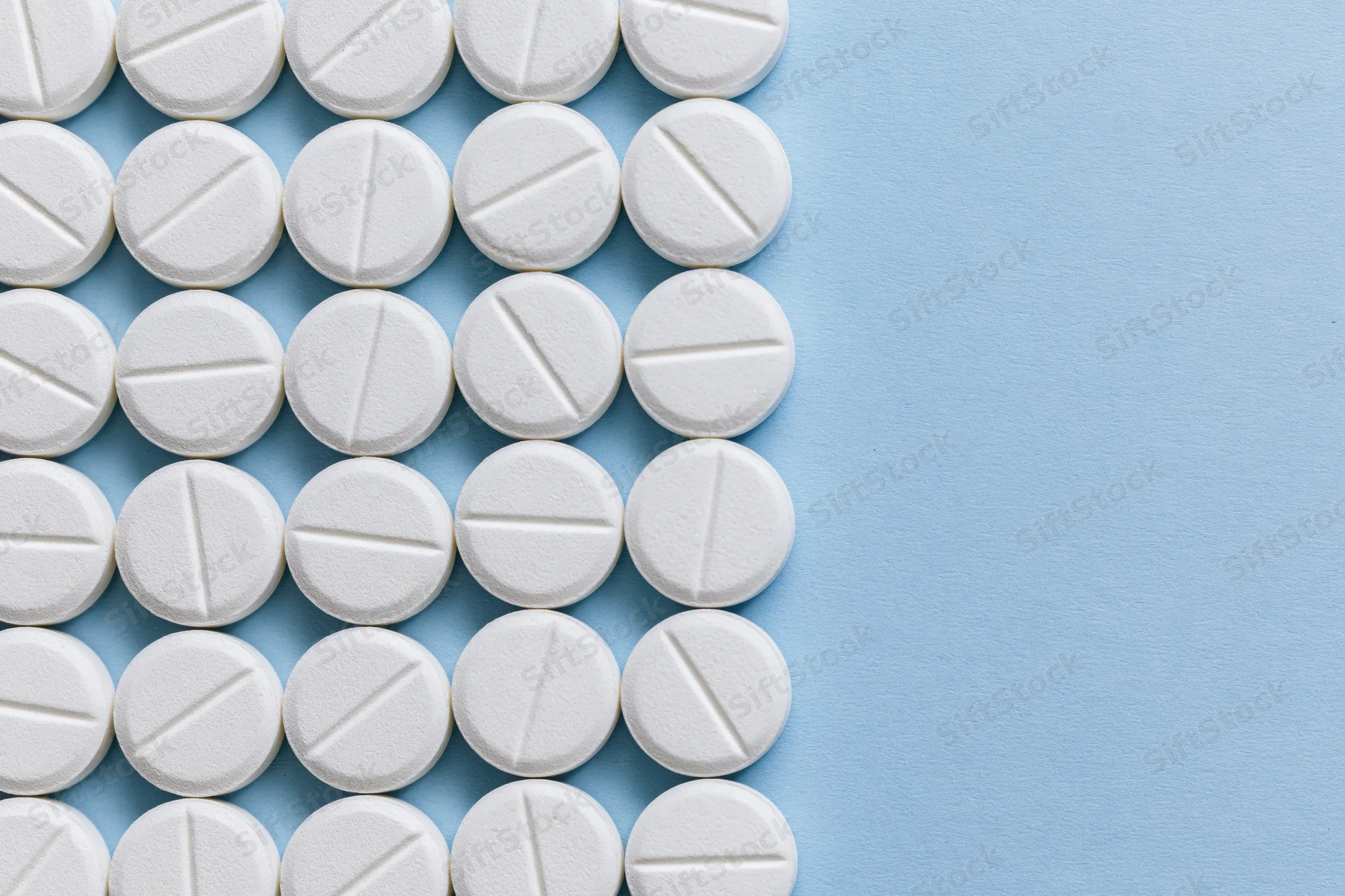 White scored tablets arranged in a grid on a blue surface with copyspace on the right