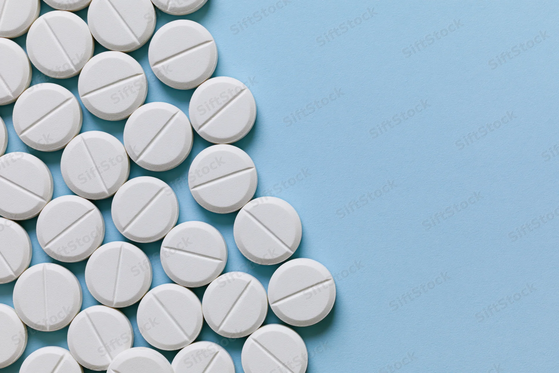White scored tablets arranged in a grid on a blue surface with copyspace