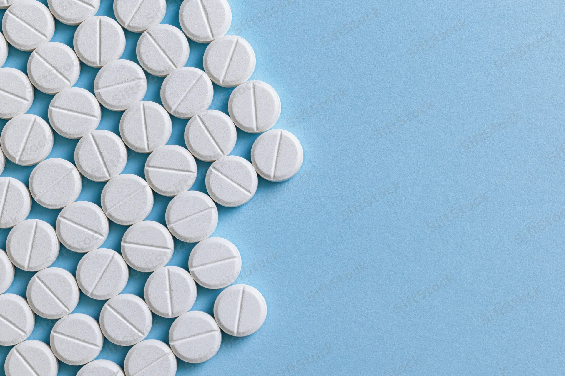 White scored tablets arranged in a grid on a blue surface with copyspace