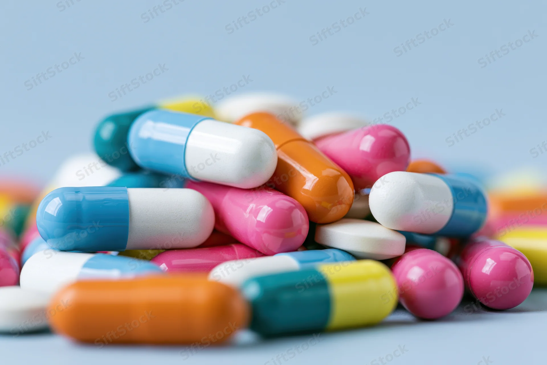 Colorful pharmaceutical capsules and pills piled on a light blue surface