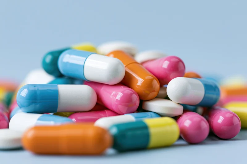 Colorful pharmaceutical capsules and pills piled on a light blue surface