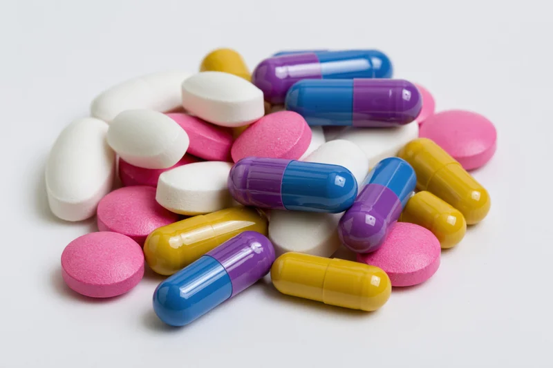 Scattered prescription pills and capsules on white surface