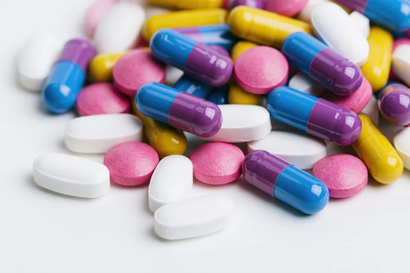 Scattered prescription pills and capsules on white surface