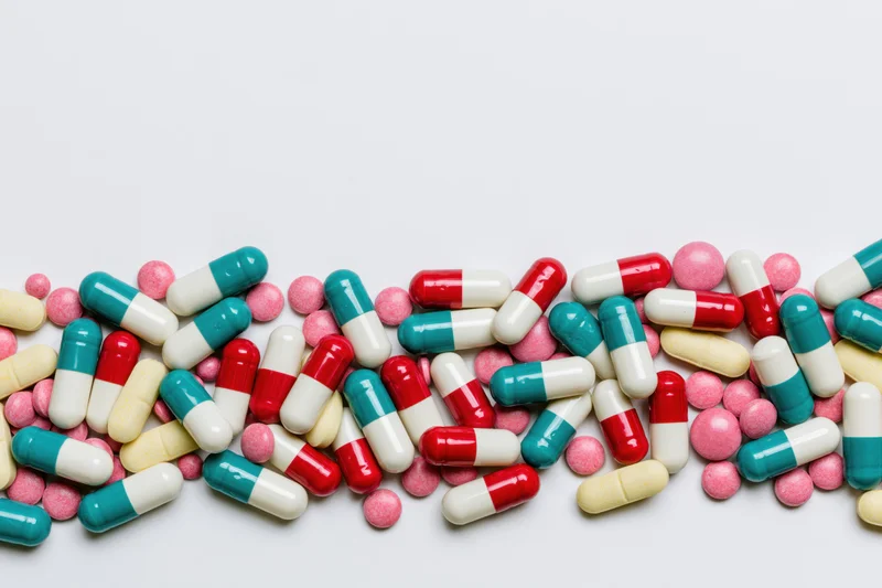 Scattered pharmaceutical capsules and pills arranged in a horizontal band across a white surface