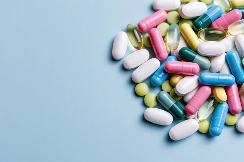 Scattered pharmaceutical pills and capsules on a blue surface with copyspace