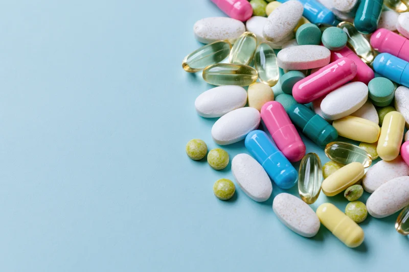 Scattered pharmaceutical pills and capsules on a blue surface with copyspace