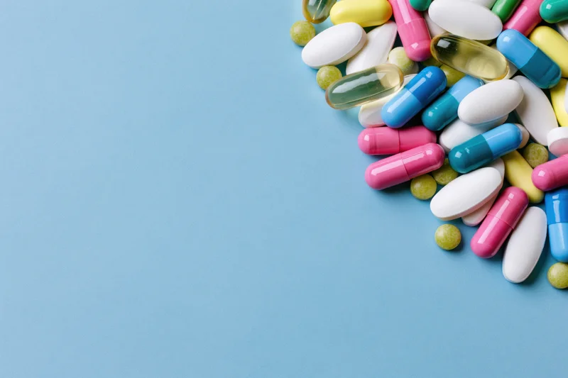 Scattered pharmaceutical pills and capsules on a blue surface with copyspace