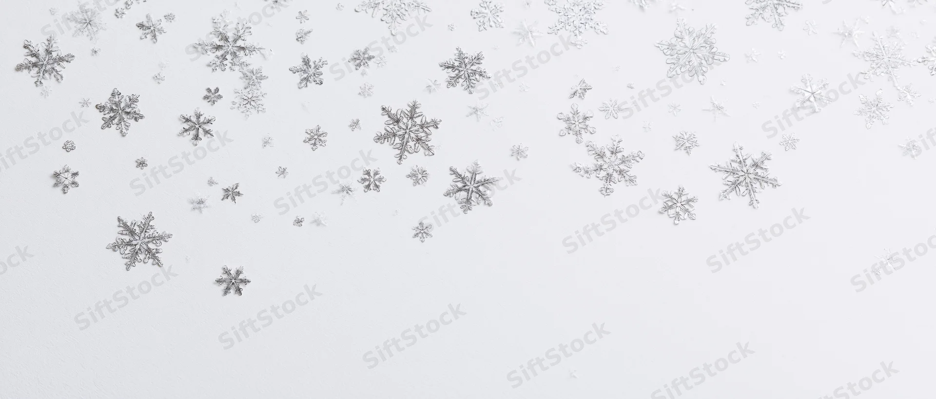 Scattered silver snowflakes drifting across a white background with copyspace