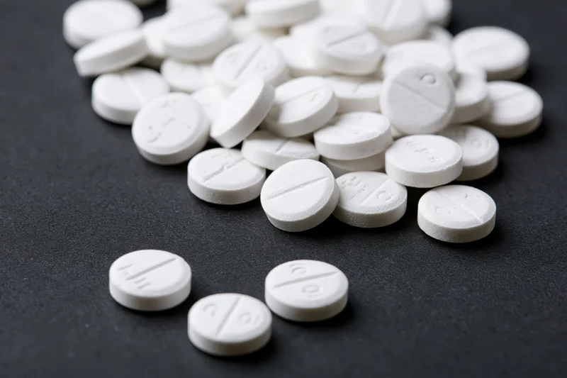 Scattered white tablets with score lines on dark surface