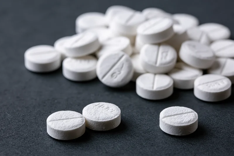 Scattered white scored tablets on dark surface