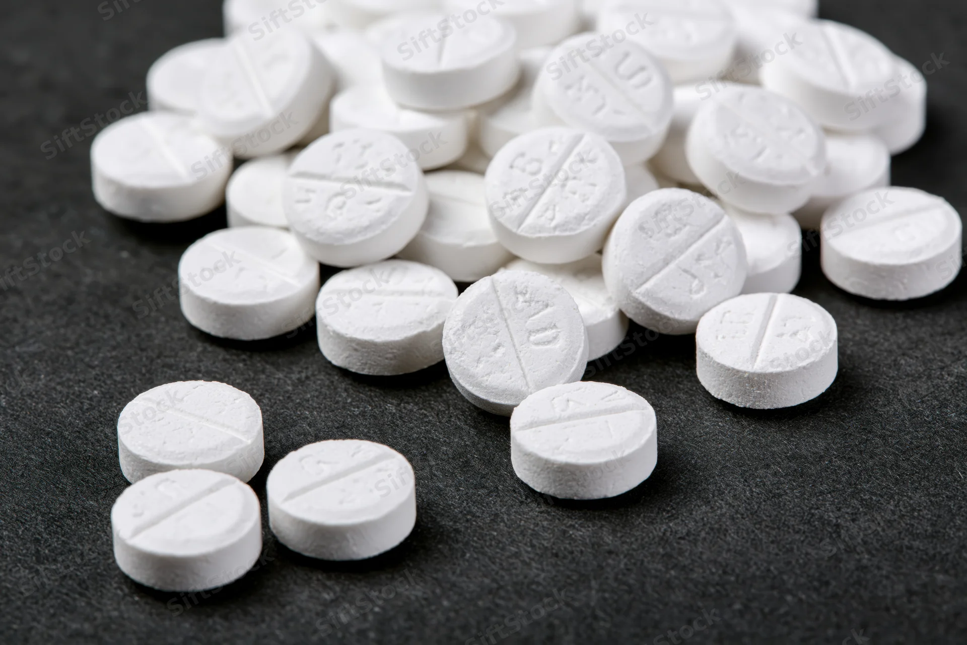 Scattered white scored tablets on dark surface