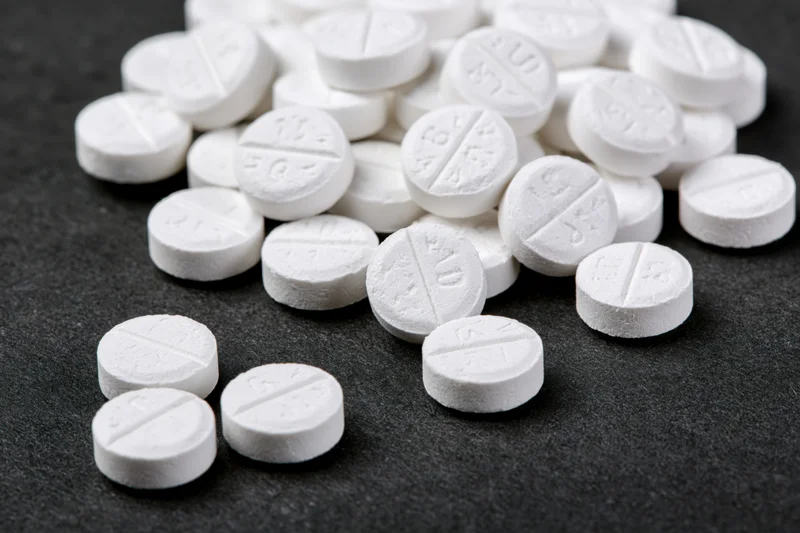 Scattered white scored tablets on dark surface