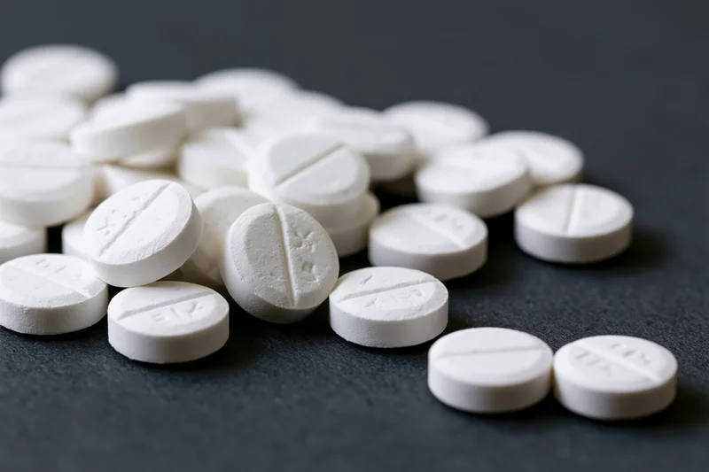 Scattered white scored tablets on dark surface
