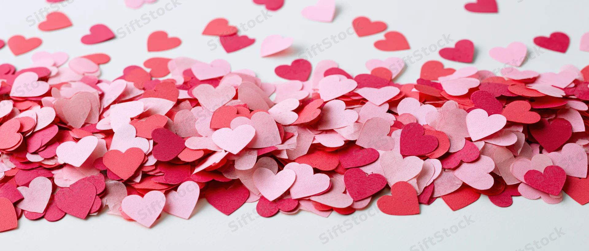 Scattered paper heart confetti in pink and red tones on white surface
