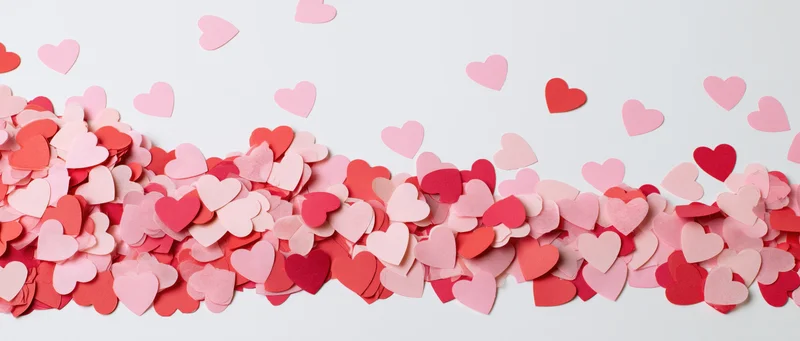 Scattered paper heart confetti in pink and red tones on white background