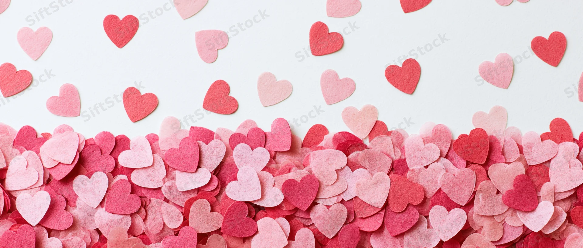 Scattered pink and red paper heart confetti arranged in a cluster on white surface with copyspace