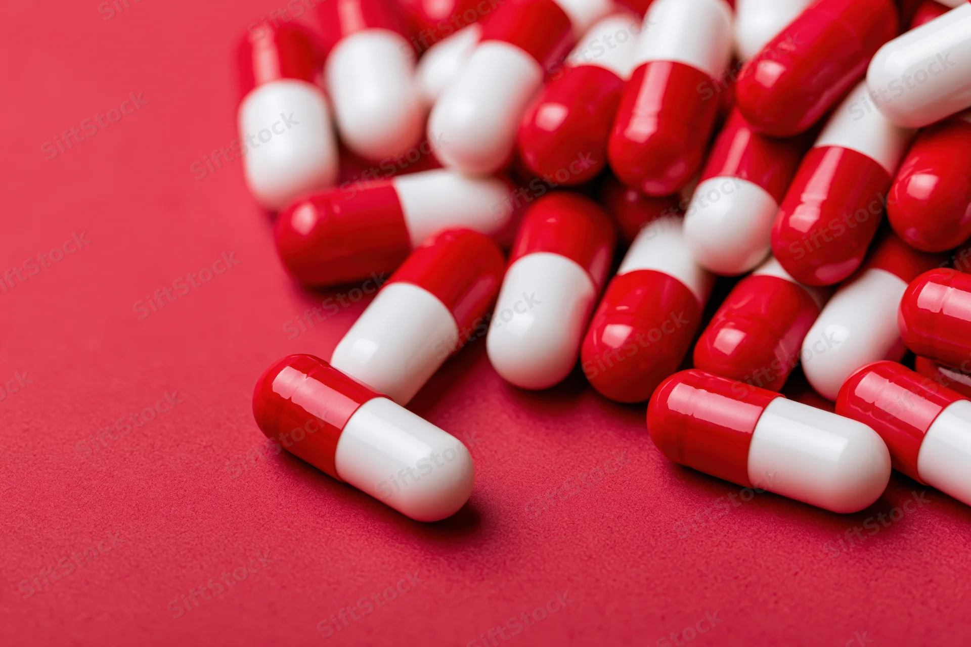 Scattered red and white two-tone capsule pills on a red surface