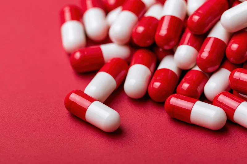 Scattered red and white two-tone capsule pills on a red surface
