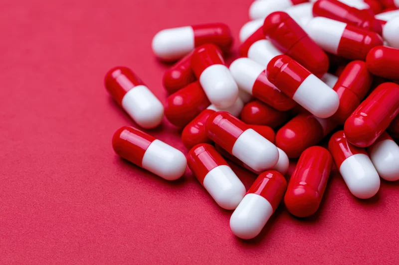 Scattered red and white two-tone capsule pills on a red surface