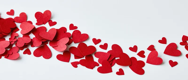 Scattered red paper heart confetti on white background with copyspace