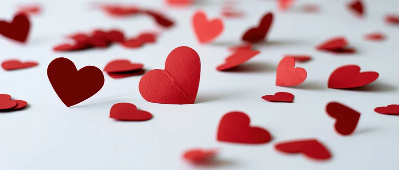 Red paper heart cutouts scattered across a white surface with shallow depth of field