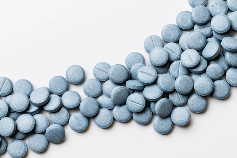 Blue coated tablets scattered across a white surface in a loose diagonal pattern