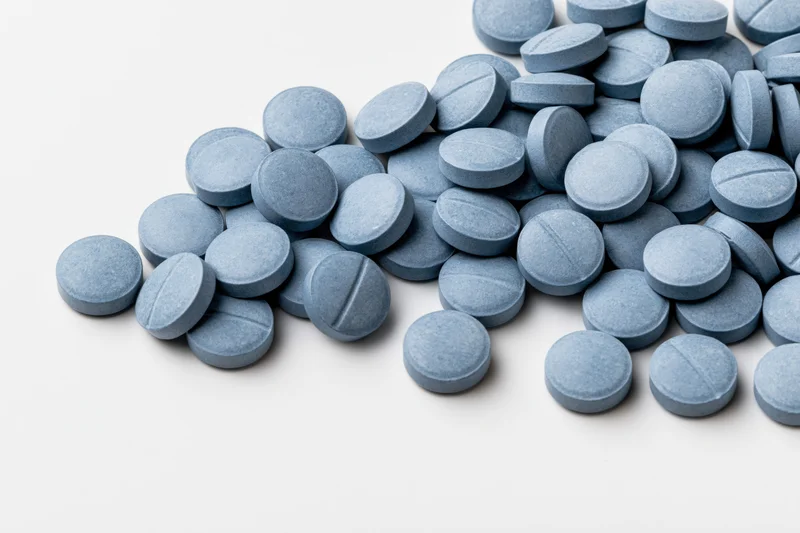 Scattered blue coated tablets arranged loosely on white surface