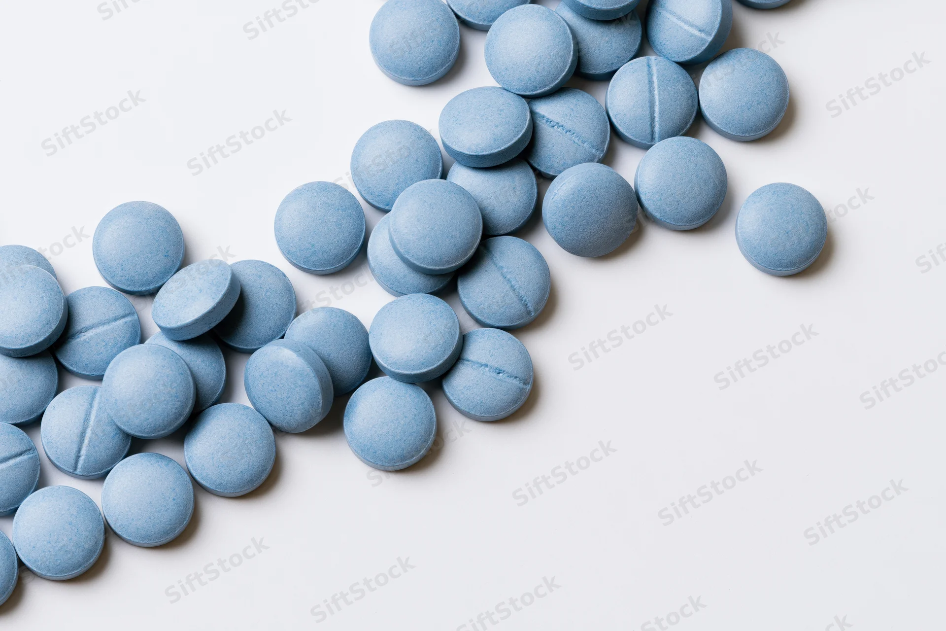 Scattered blue coated tablets on white surface