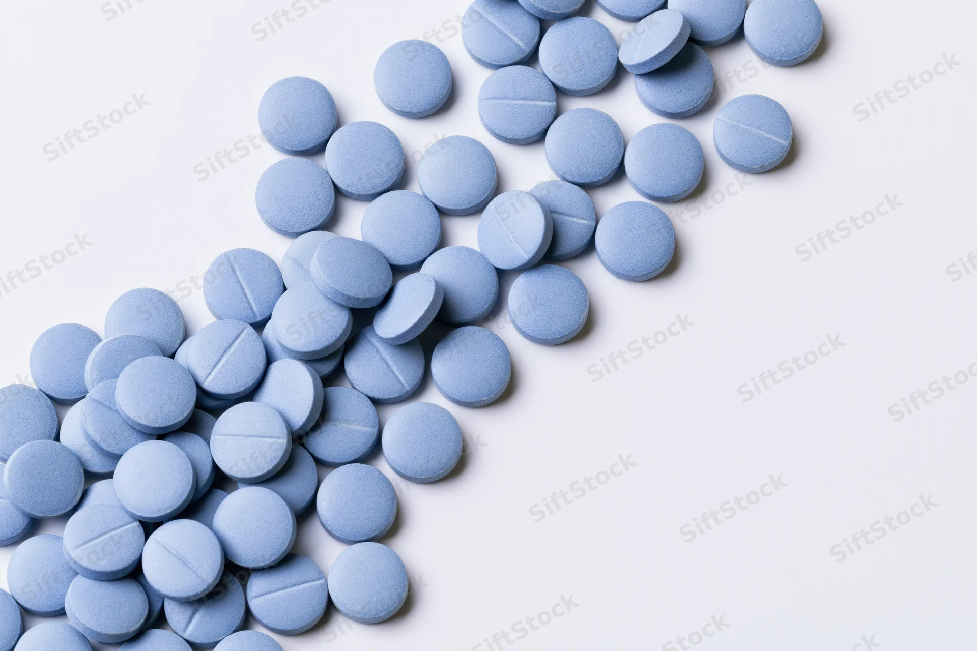Scattered blue coated tablets on white background with copyspace