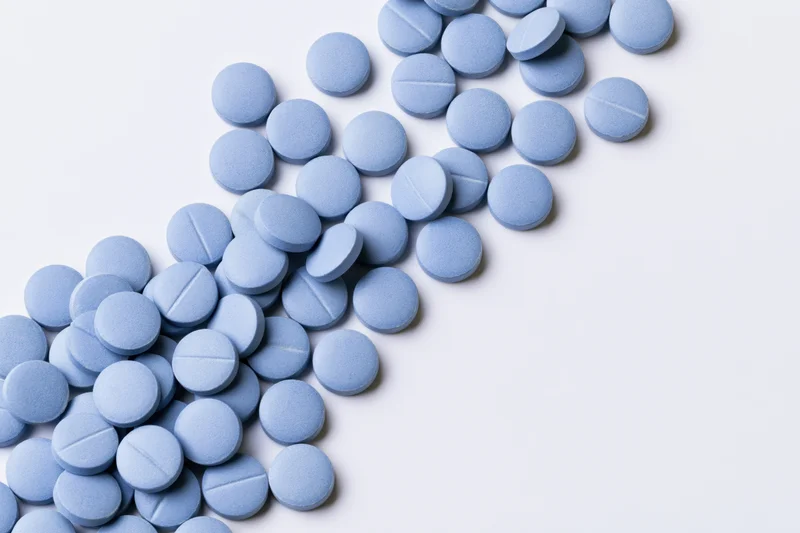 Scattered blue coated tablets on white background with copyspace