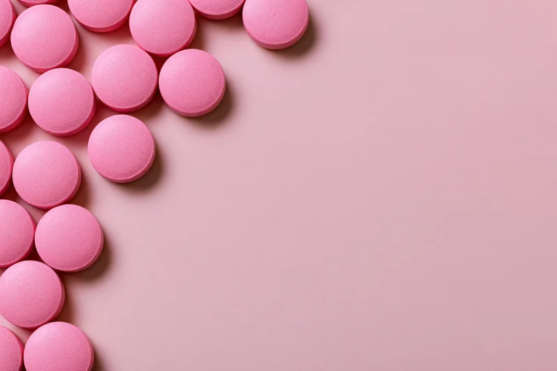 Scattered round pink supplement pills arranged loosely along the left edge on a pink surface with copyspace