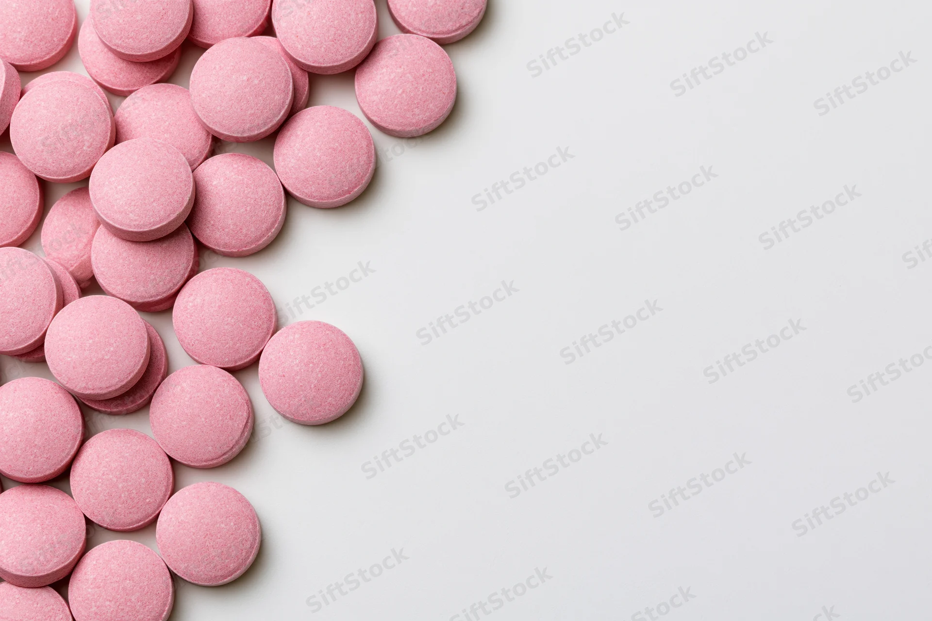 Scattered round pink supplement pills arranged loosely along the left side of a white surface