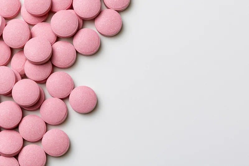 Scattered round pink supplement pills arranged loosely along the left side of a white surface