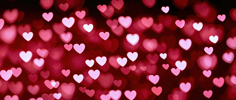 Scattered heart-shaped bokeh lights in red and pink hues against a dark background