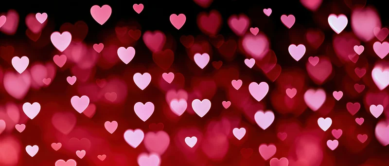 Scattered heart-shaped bokeh lights in red and pink hues against a dark background