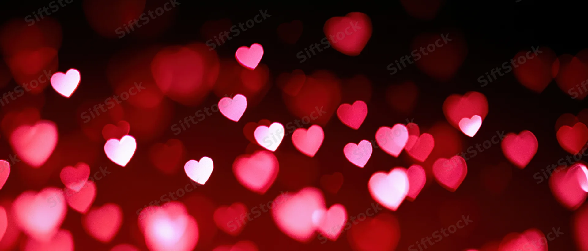 Scattered heart-shaped bokeh lights in red and pink against a dark background
